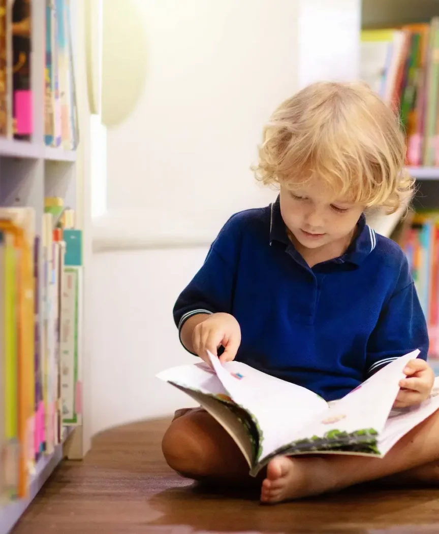 A young student reading beside a bookshelf