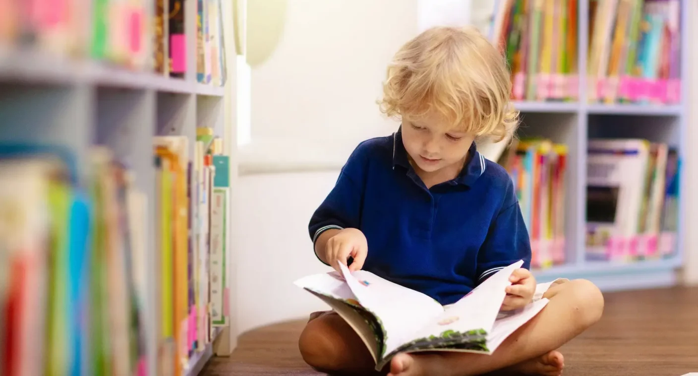A young student reading beside a bookshelf