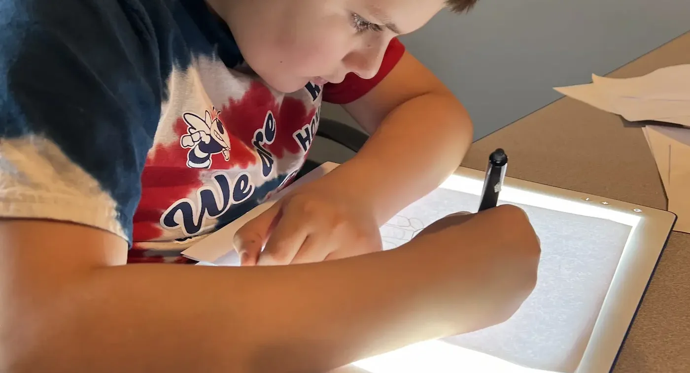 A student writing over a light box in class