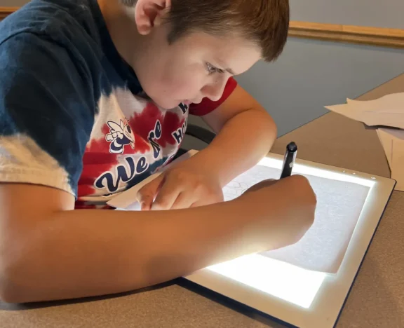A student writing over a light box in class